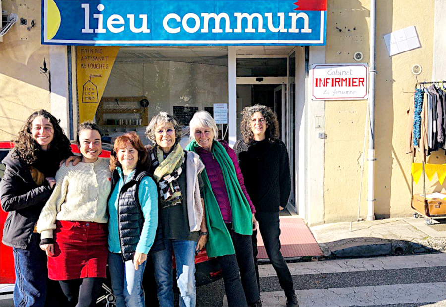 Six femmes posent devant le local ayant pour enseigne « lieu commun ». À droite de l’entrée, une pancarte indique « Cabinet infirmier La Gervanne ». Sur la vitrine, à gauche de l’entrée, sont listés les mots suivants : – friperie ; – artisanat ; – retouches.
